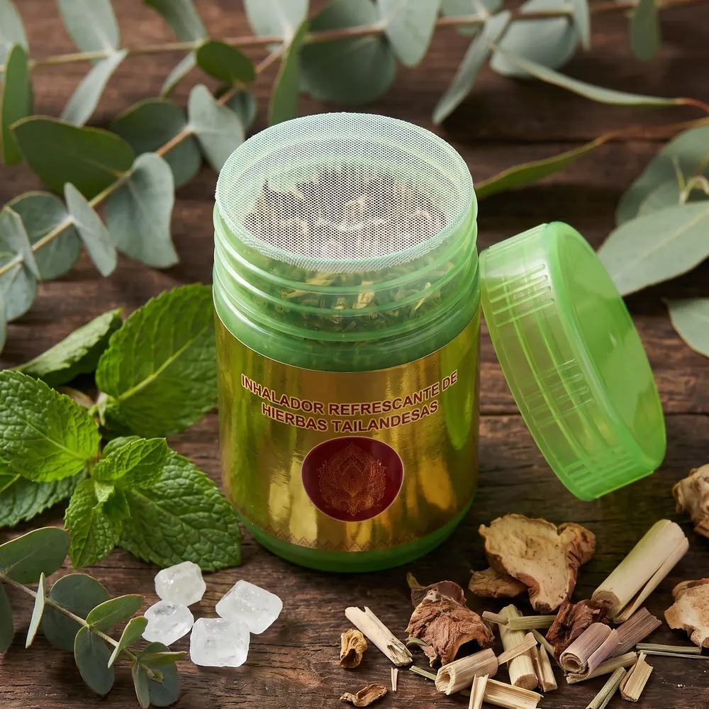 Inhalador tailandés abierto, con el sello de malla y las hierbas dentro, rodeado de menta, eucalipto y alcanfor